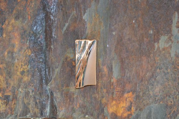 Goldglänzende Brosche auf Stein Eine goldglänzende Brosche in rechtreckiger Form liegt auf einem Stein